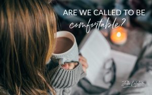 Are We Called to Be Comfortable? | woman in comfy sweater with hot chocolate looking at a book and lit candle