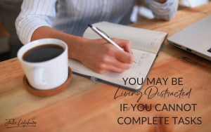 You May Be Living Distracted if You Cannot Complete Tasks | woman sitting at wooden desk writing a list in a book next to a white cup of coffee